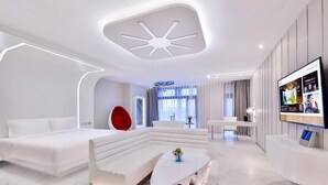 Une chambre d’hôtel moderne avec un canapé blanc, un fauteuil rouge, une table basse blanche et un téléviseur fixé au mur.