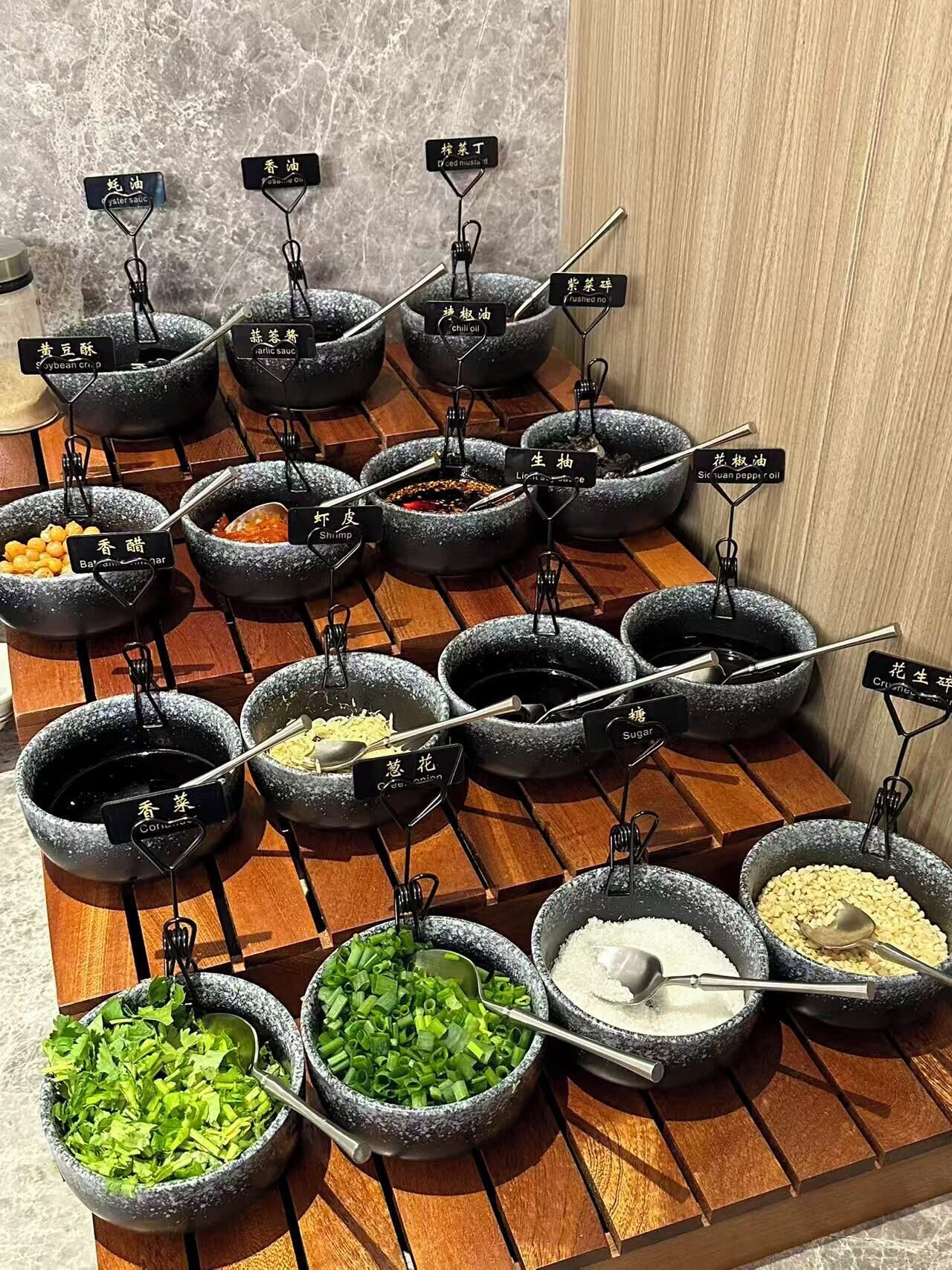 A variety of condiments and sauces arranged in stone bowls on a wooden rack.