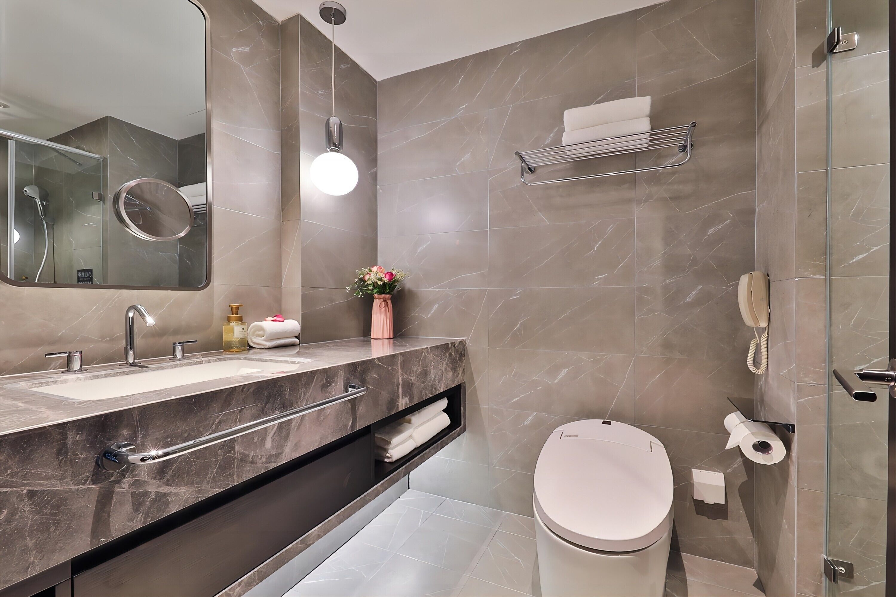 Un baño moderno con lavamanos doble, inodoro, cabina de ducha con mampara de vidrio y perchero para toallas.