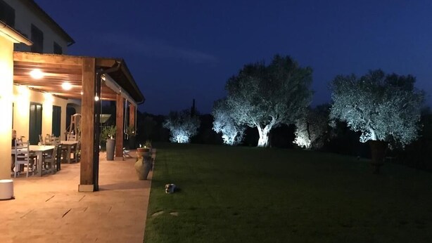A patio area with a wooden pergola, outdoor seating, and a well-lit garden with trees. - Villa with pool in Capalbio 6 rooms 6 bathrooms immersed in olive grove (Toscana)