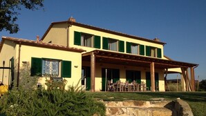 A two-story building with a covered patio area, stone steps leading to the entrance, and a grassy foreground. - Villa with pool in Capalbio 6 rooms 6 bathrooms immersed in olive grove (Toscana)