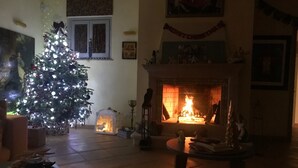 A warmly lit living room with a Christmas tree, a fireplace, and a dining table. - Villa with pool in Capalbio 6 rooms 6 bathrooms immersed in olive grove (Toscana)