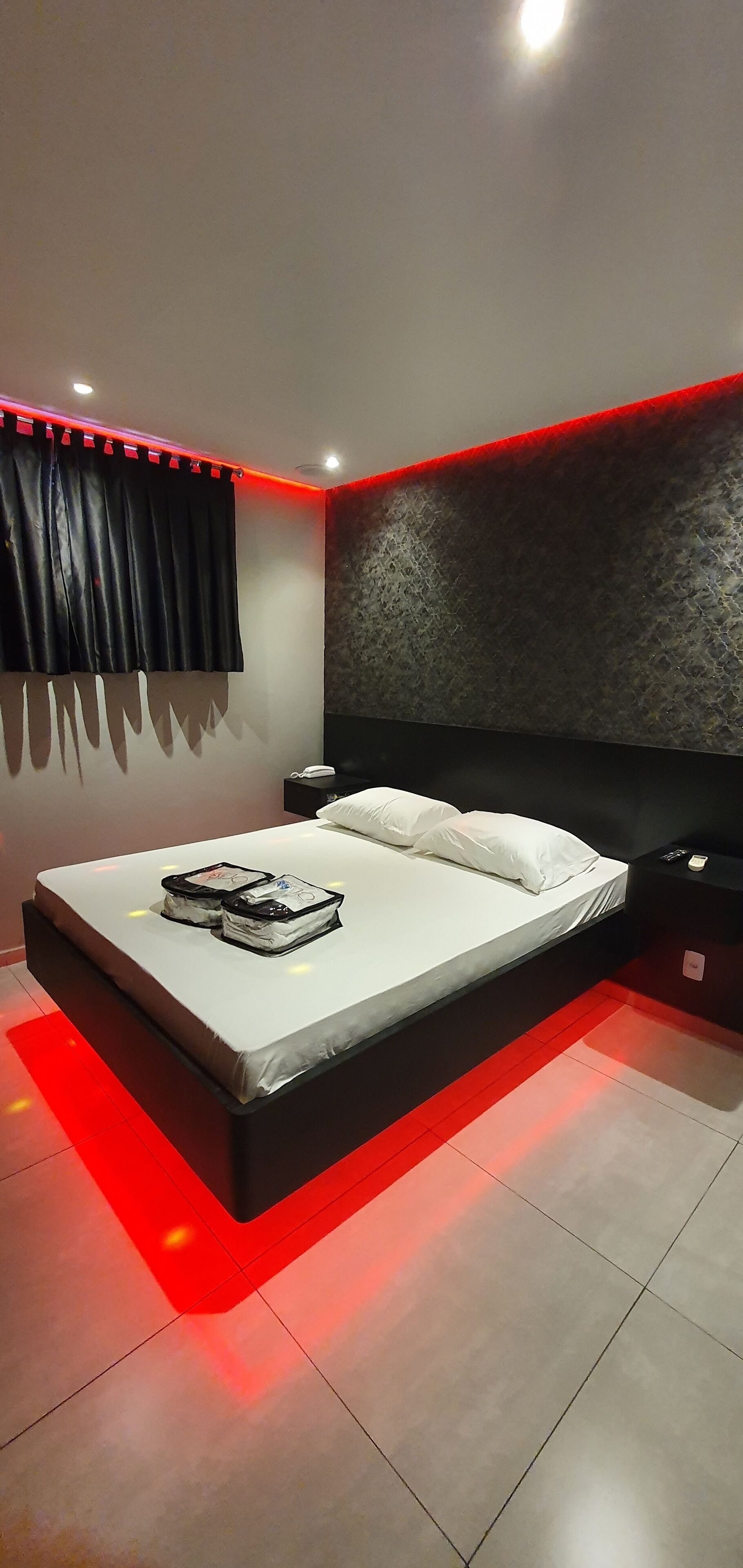 Une chambre moderne avec un grand lit, une tête de lit au motif texturé et un éclairage d’ambiance rouge.