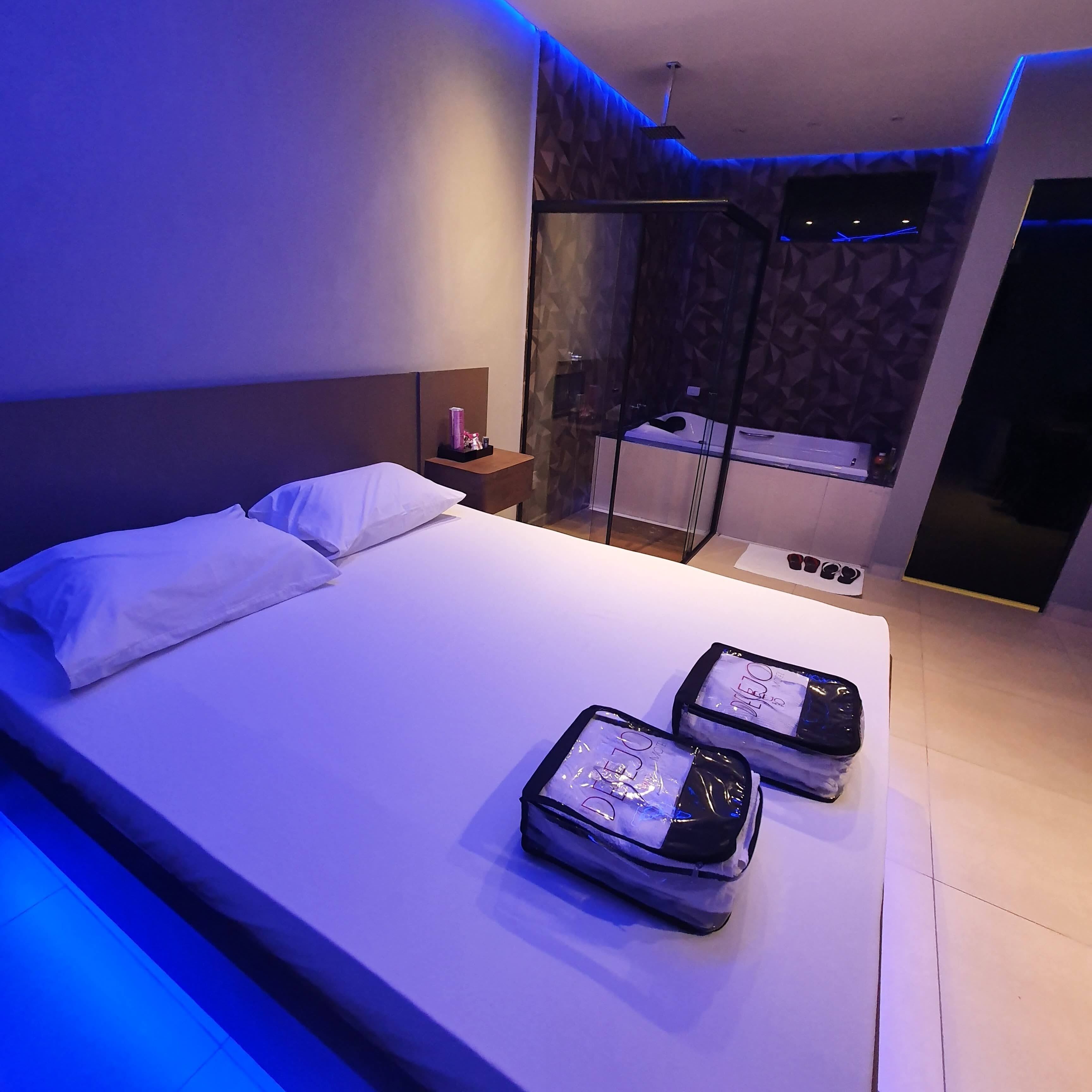 Une chambre moderne avec un grand lit, une table de chevet et une salle de bain visible à travers une cloison en verre.
