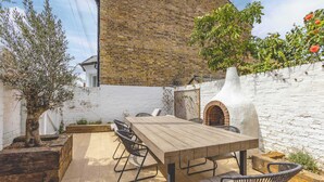 An outdoor patio with a wooden table and chairs, a brick wall, and a white fence. - Stylish 3 Bdr Home Central Windsor By Tempstay (Berkshire)