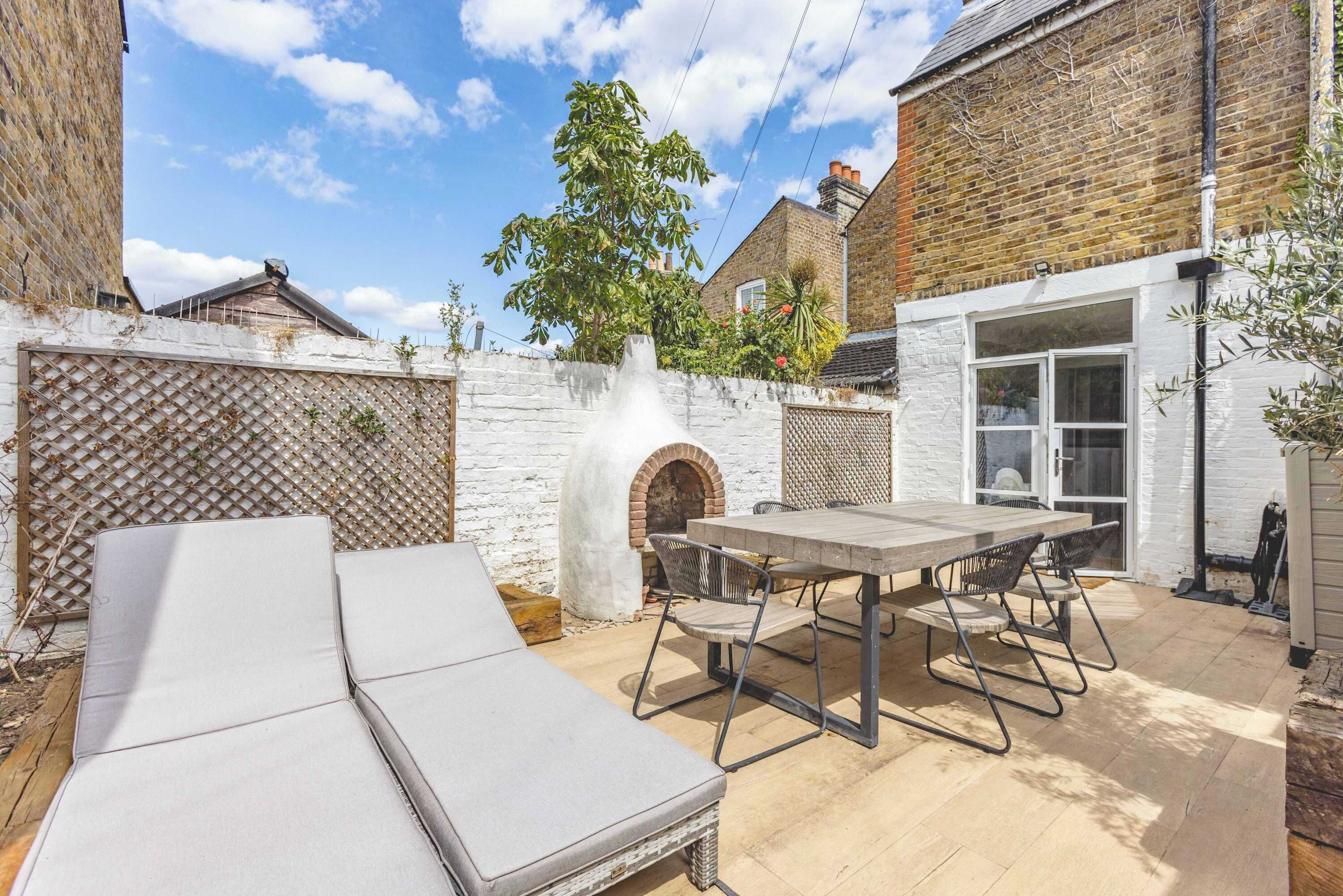 A patio with a table and chairs, a brick oven, and a white wall.
