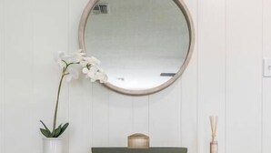 A wooden console table with a round mirror above it, a potted orchid, and a small box on the table.