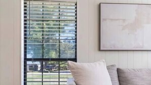 A room with a grey sofa, a round wooden side table, and a window with blinds.
