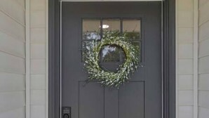 A gray front door with a wreath and a small window above it.