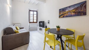Una sala de estar moderna con un sofá, una mesa de comedor con sillas, un televisor y un cuadro en la pared.