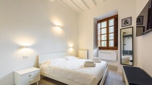 Un dormitorio con cama, mesita de noche, luz empotrada en la pared, ventana y espejo.