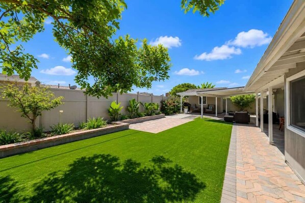 A backyard with a well-maintained lawn, a patio area with outdoor furniture, and a covered seating area. - Disneyland 5BR/3BA Lux Villa, Arcade & Billiards (Anaheim)