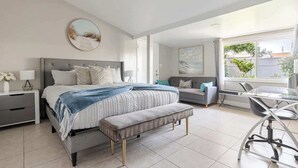 Un dormitorio moderno con cama, mesitas de noche, un banco, un escritorio y una silla.