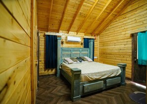 Cozy cabin with a bed, wooden headboard, and air conditioning unit, set against a sloped ceiling with wooden beams.