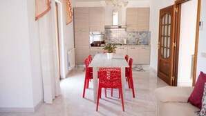 Een moderne keuken met lichte kasten, een centraal eiland met een spoelbak, en een eethoek met rode stoelen.
