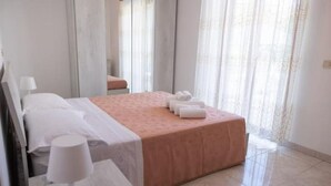 Een hotelkamer met een bed, een nachtkastje met een lamp en een raam met gordijnen.