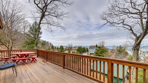 Um deck de madeira com mesas e cadeiras para piquenique, com vista para uma área residencial e um corpo d'água.