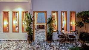 Un espace intérieur accueillant, doté d’un sol à motifs, d’un coin salon avec une table et des chaises, et d’un mur décoratif orné d’un motif géométrique.