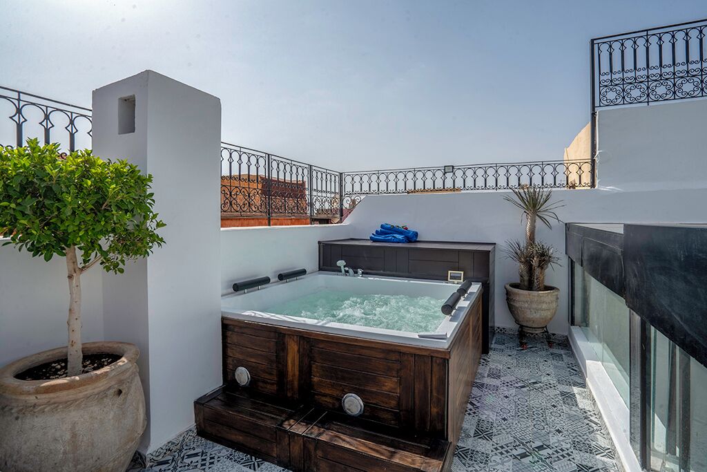 A rooftop terrace with a hot tub, potted plants, and a patterned floor.
