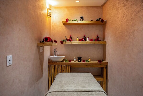 A spa room with a wooden bench, a sink, and shelves with toiletries and flowers.