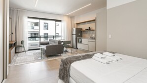 A modern hotel room with a large bed, a sofa, a dining area, and a kitchen. - WI-FI 200MB | Me2 Benefits | Foodhall #TS1 (Florianópolis)
