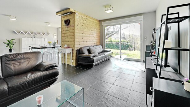 Un salon moderne avec un canapé en cuir, une table basse en verre, un mur d’accent en bois et un coin cuisine comprenant une table à manger et des chaises.