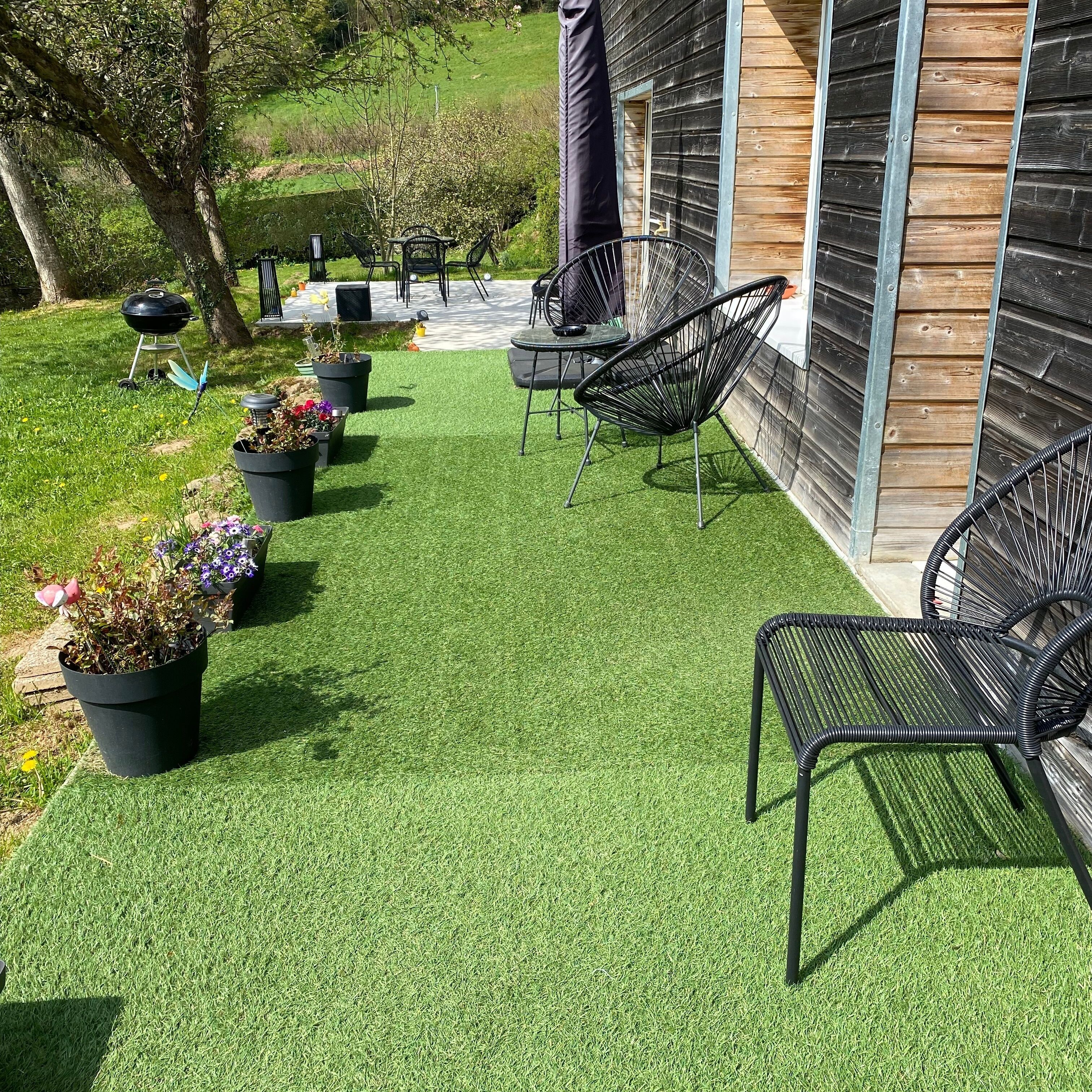 Een terras met kunstgras, buitenmeubels en potplanten.