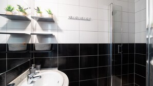 Un baño moderno con un lavamanos blanco, paredes con azulejos blanco y negro, un box de ducha de vidrio y plantas en estantes.