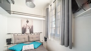 Un dormitorio moderno con cama, cabecera, mesita de noche, lámpara y ventana con cortinas.