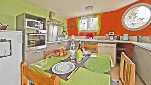 Une cuisine compacte équipée d’un four à micro-ondes, d’une cuisinière et d’un évier. On y trouve une table à manger avec des chaises, ainsi qu’une fenêtre avec des rideaux.