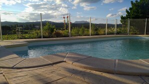 Une piscine dotée d’une plage en pierre, entourée d’une clôture en métal et de verdure.