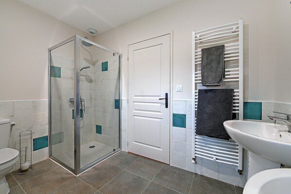 A bathroom with a glass-enclosed shower, a white door, a towel rack, and a sink.