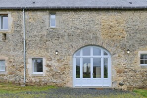 A stone building with a large arched window and smaller windows, a metal pipe, and a lamp post.