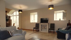 Ein Wohnzimmer mit grauem Sofa, einem Holztisch, einem Kamin und einem Fernseher auf einem Schrank.