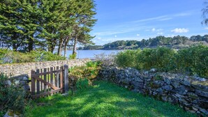 A stone wall with a wooden gate leading to a grassy area with trees and a view of a lake.
