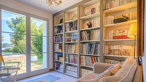 A cozy reading nook with a large bookshelf filled with books, a comfortable sofa, and a view of the outdoors through a glass door.