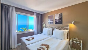 Une chambre d’hôtel avec deux lits, une grande fenêtre donnant sur un beau paysage et un mur orné de deux tableaux encadrés.