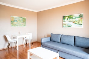 Sala de estar com sofá azul, mesa de centro branca e duas cadeiras brancas. Há duas pinturas emolduradas nas paredes.