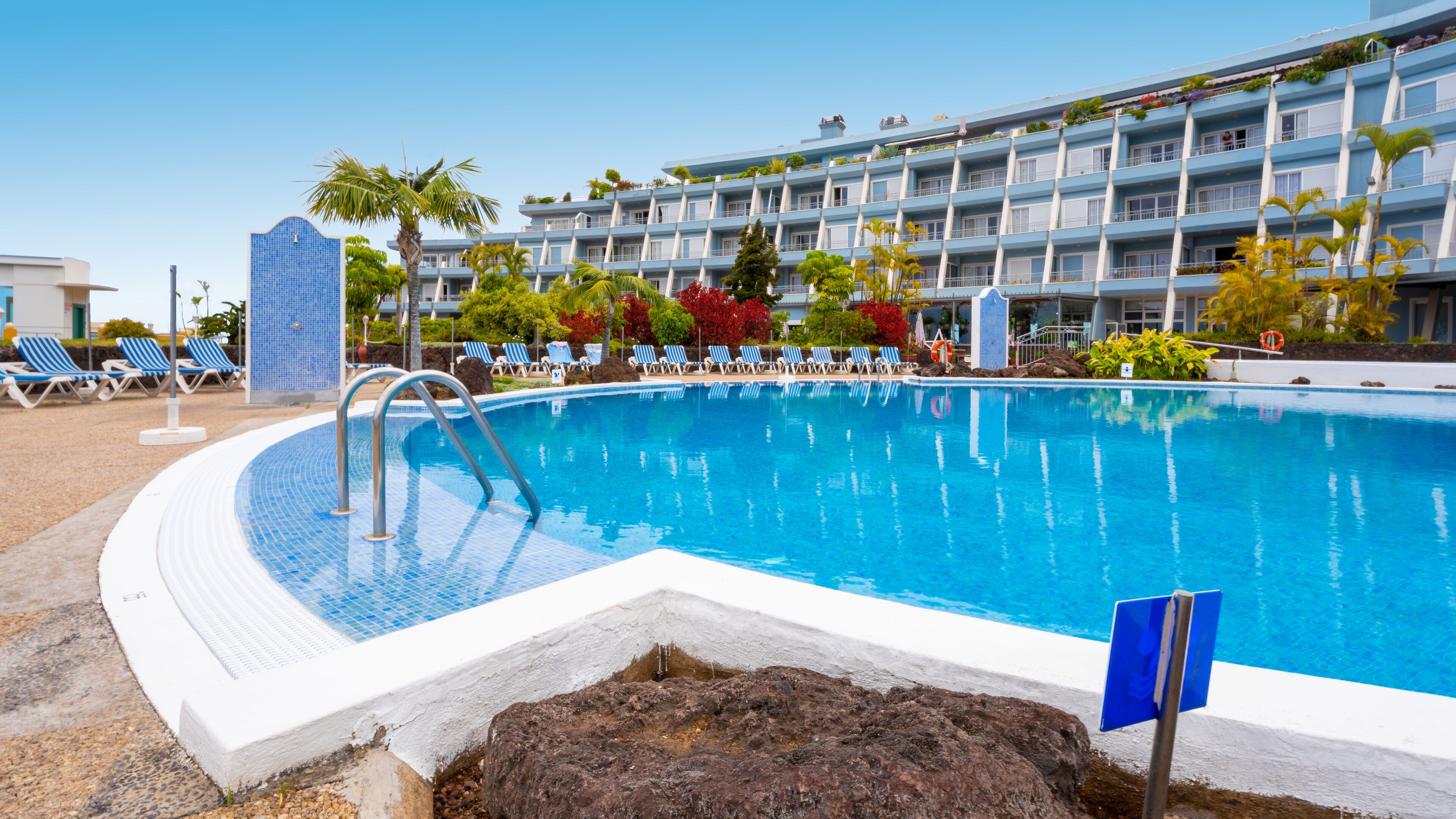 Une piscine avec des chaises longues et, au fond, le bâtiment de l’hôtel.