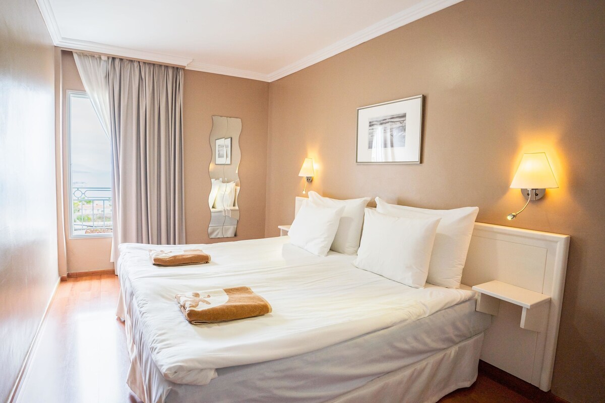 Une chambre d’hôtel avec deux lits, une fenêtre avec des rideaux, une lampe fixée au mur et un tableau encadré.