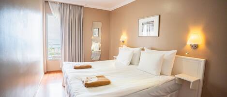 A hotel room with two beds, a window with curtains, a wall-mounted lamp, and a framed picture.