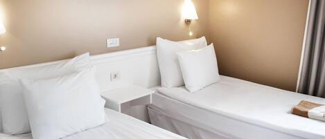 A hotel room with two beds, a nightstand, a wall-mounted lamp, and a framed picture on the wall.
