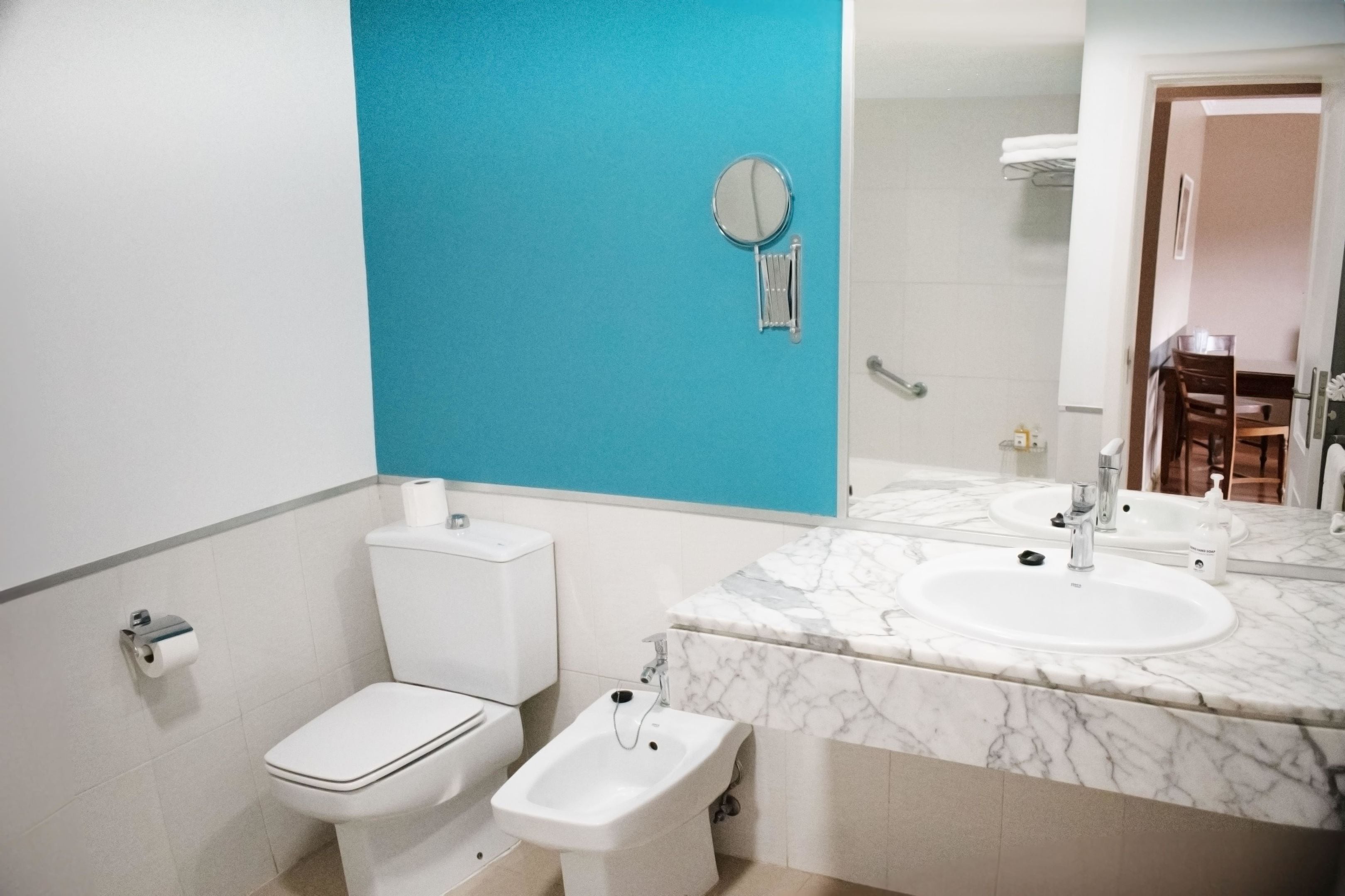 Une salle de bain comprenant des toilettes, un bidet, un lavabo, un miroir et un mur d’accent bleu.