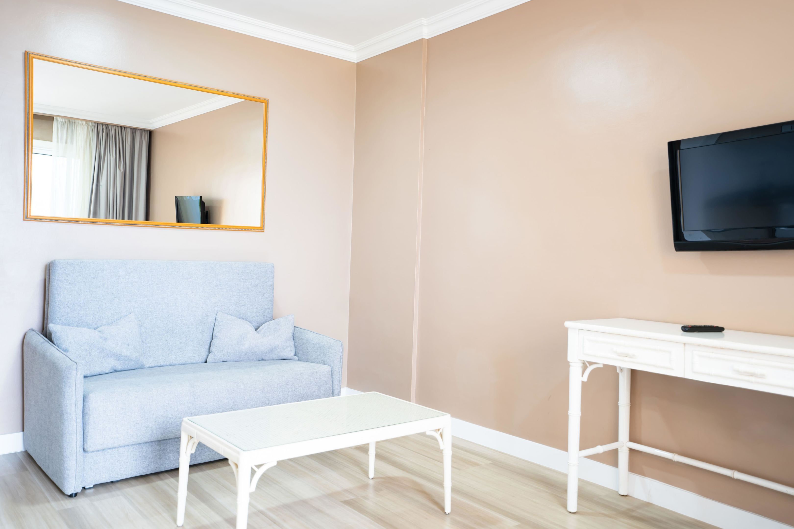 A room with a light blue sofa, a white coffee table, a white desk, and a flat-screen TV mounted on the wall.
