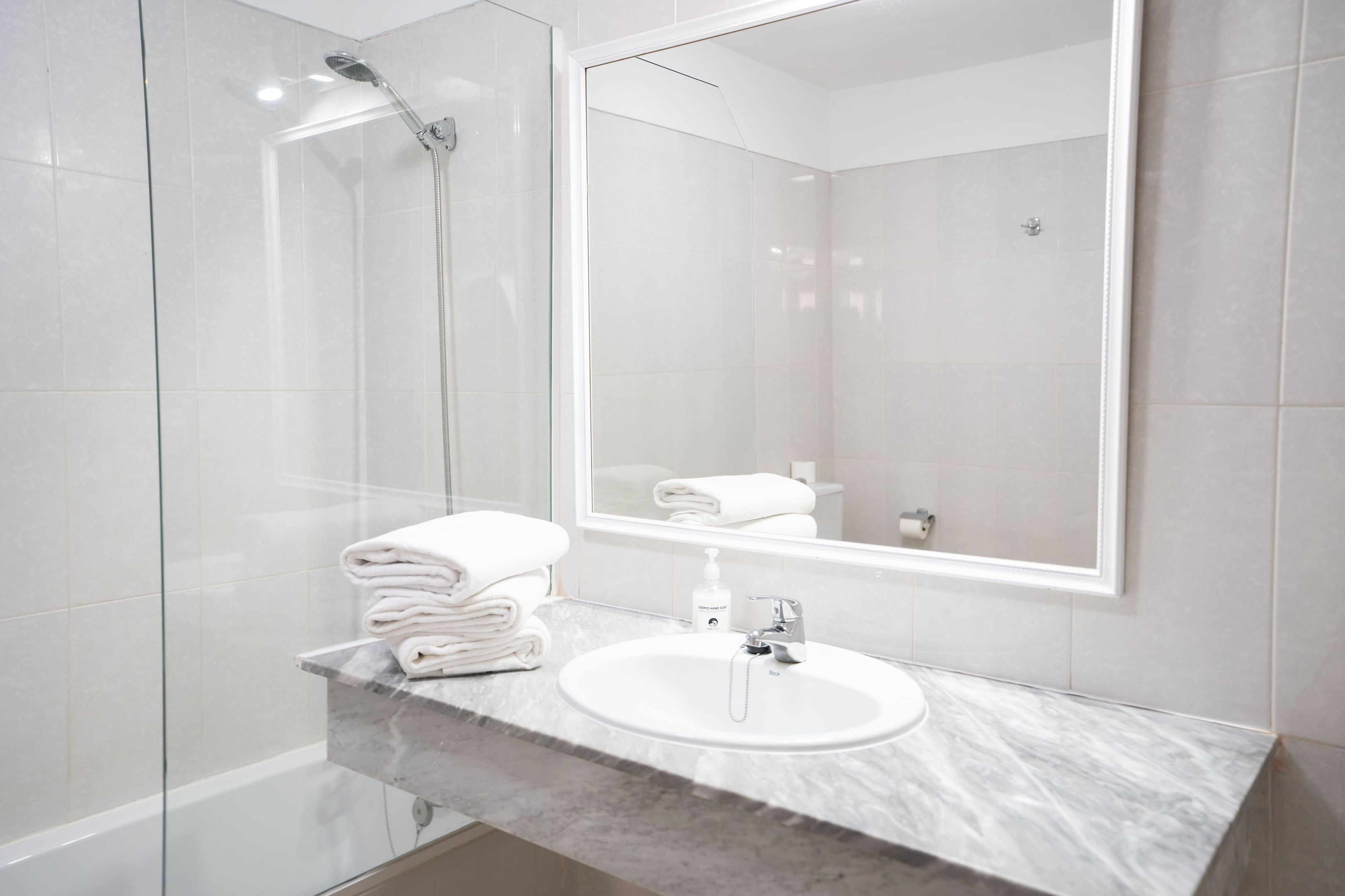 A modern bathroom with a glass shower enclosure, a marble sink, and a large mirror.