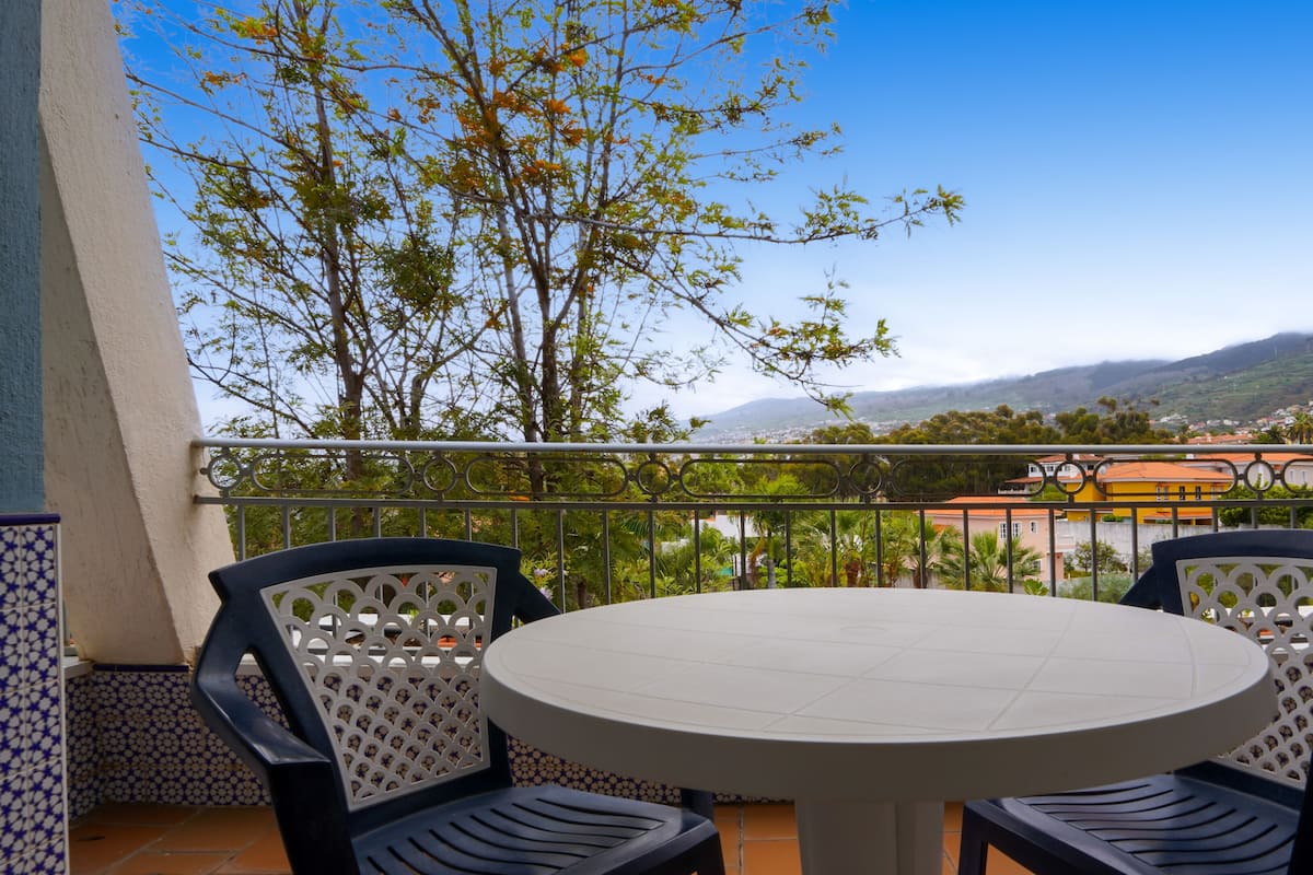 Un balcon avec une table ronde et deux chaises, offrant une vue panoramique sur une ville et des collines.