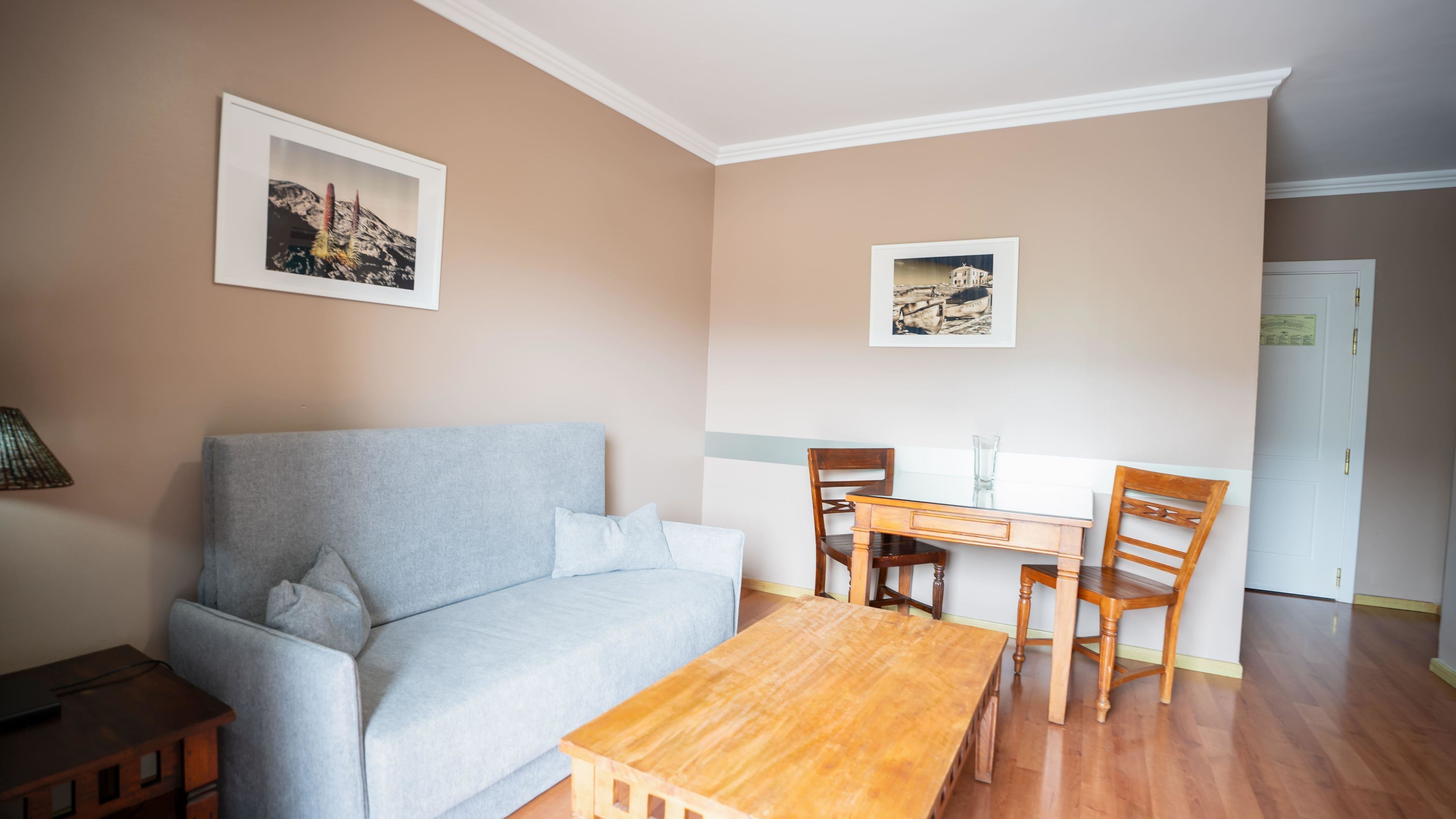 Una sala de estar con un sofá, una mesa de centro de madera, una mesa de comedor con sillas y dos cuadros en la pared.
