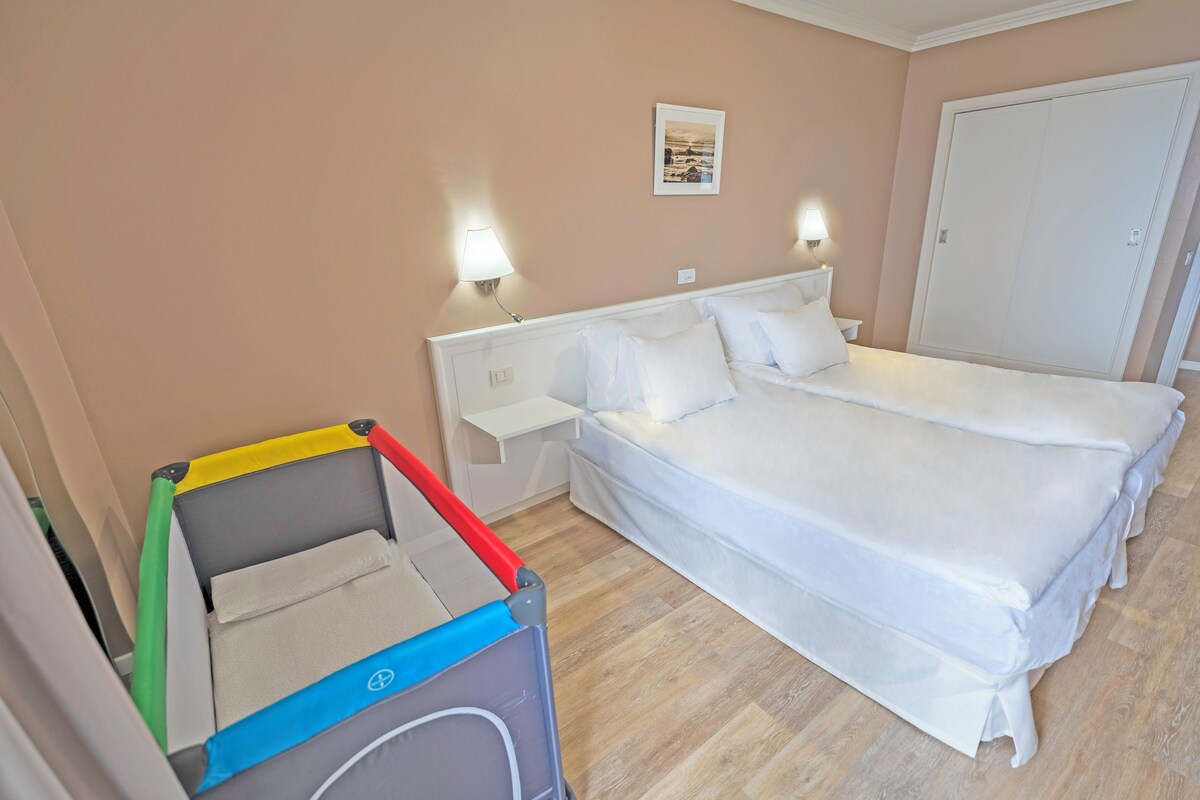 Une chambre d’hôtel avec deux lits, une table de chevet, une lampe fixée au mur et une grande armoire.