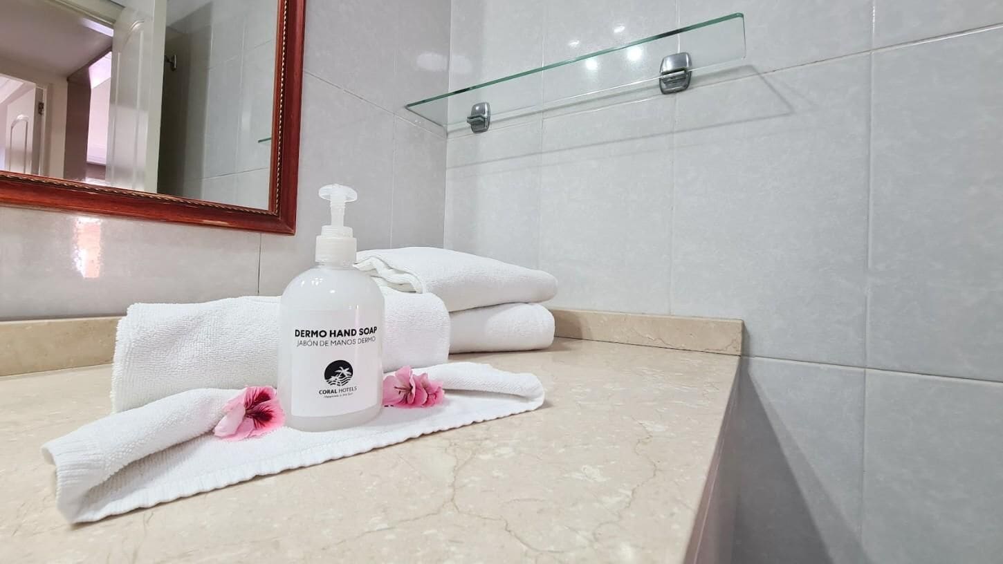 A bathroom with a marble countertop, a hand soap dispenser, folded towels, and a glass shelf.
