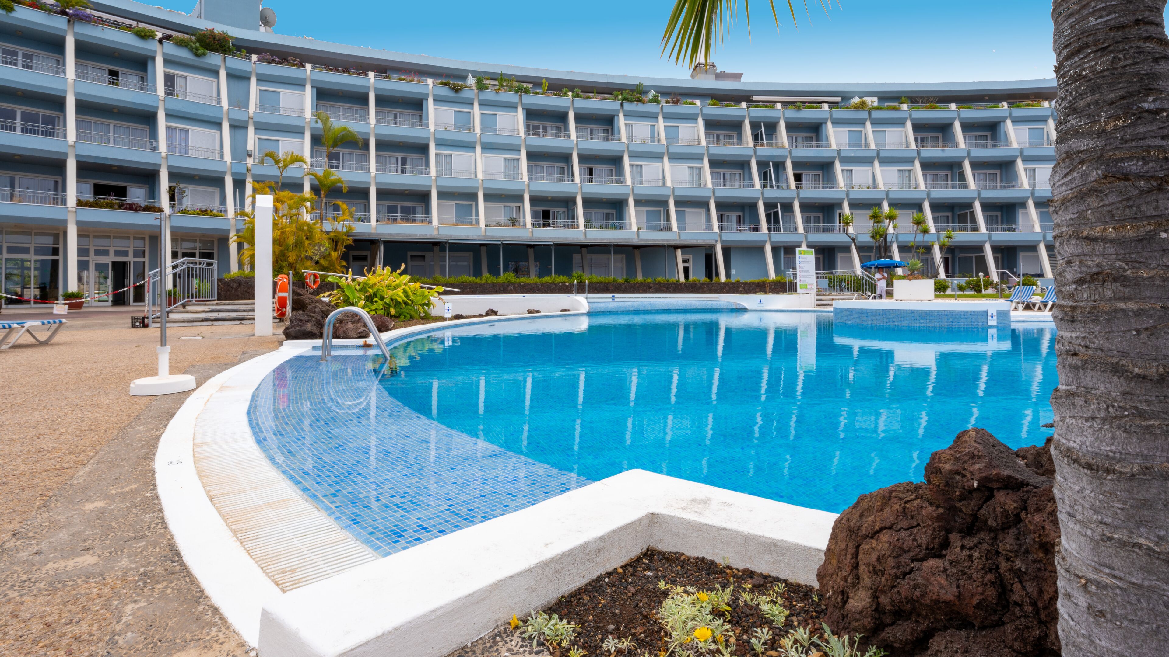 Un hôtel doté d’une grande piscine, de nombreux balcons et d’un palmier.